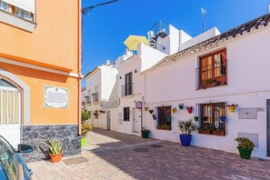 A narrow street with white buildings, potted plants, and a clear blue sky. - Coral8 - Top modern townhouse in Estepona old town (Estepona)