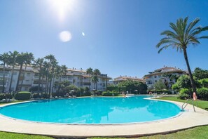Ein großer Pool im Freien, umgeben von Palmen und einem mehrstöckigen Gebäude mit Balkonen.