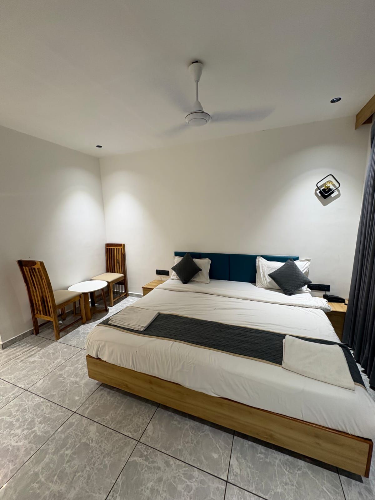 A hotel room with a bed, a desk, a chair, a ceiling fan, and a wall-mounted light fixture.