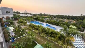 A swimming pool surrounded by greenery, with a checkered deck area and a covered seating area.