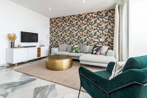 Una sala moderna con un sofá, una mesita redonda y un televisor sobre un mueble blanco.
