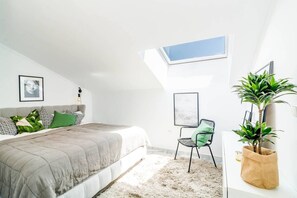 Un dormitorio con tragaluz, una cama con ropa de cama estampada, una silla y una planta en maceta.