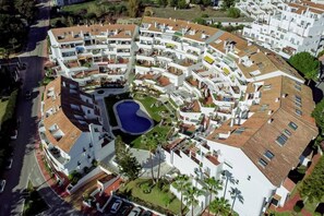 A high-rise residential building with multiple balconies, a central courtyard with a swimming pool, and a surrounding landscaped area. - ELD2-Luxury 3 Bedroom Penthouse in Nueva Andalucia (Marbella)
