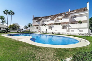 A pool area with a clear blue pool, surrounded by a white building with a tiled roof and a grassy lawn. - ELd41- Prime location, pool views and evening sun (Marbella)