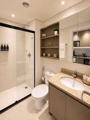 Un bagno moderno con cabina doccia in vetro, un water, un lavabo con piano in granito e un mobile vanitario con specchio.