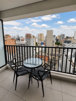 Ein Balkon mit einem Glastisch und vier Stühlen mit Blick auf eine Stadtlandschaft und verschiedene Gebäude.