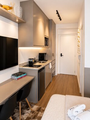 Eine moderne Küche mit Einbauofen, Mikrowelle und Spüle. Ein Essbereich mit Tisch und Stühlen sowie ein Bett mit ordentlich zusammengelegtem Handtuch.
