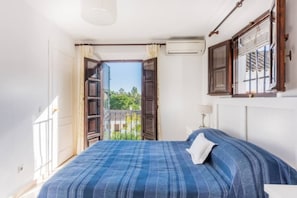 A bedroom with a bed, a window with curtains, an air conditioning unit, and a view of greenery outside. - EN- Cozy Andalusian style townhouse in Marbella (Marbella)