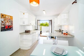 A compact kitchen with white cabinets, a dining area, and a view of greenery outside. - EN- Cozy Andalusian style townhouse in Marbella (Marbella)