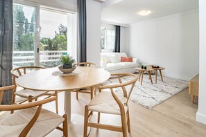 Ein modernes Wohnzimmer mit einem runden Holztisch, vier Stühlen, einem weißen Sofa und einem kleinen Beistelltisch.