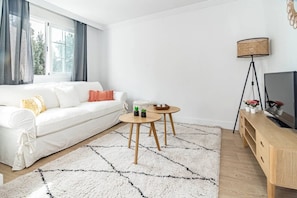 A modern living room with a white sofa, two small tables, a floor lamp, and a TV on a wooden stand. - GO- Golden Banus by Roomservices (Marbella)