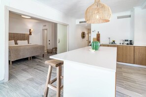 Un interior modern amb una illa central, un llit amb capçalera i una zona de cuina.