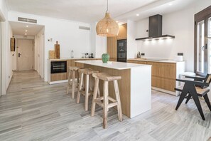 Una cuina moderna amb una illa central, tamboretes de fusta i un llum penjant.