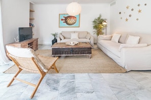 Ein Wohnzimmer mit einer Couch, einem Couchtisch, einem Korbstuhl, einem Fernseher und Wanddekoration.