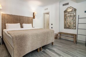 Ein Schlafzimmer mit einem Bett, einer Wandlampe, einer Bank und einem dekorativen Spiegel.