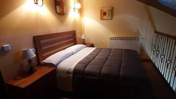 Un dormitorio con techo de madera, una cama con cubrecama oscuro, lámparas de noche y una mesita de noche.