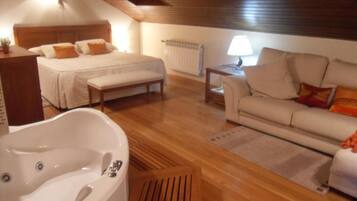 A bedroom with a large bed, a sitting area with a sofa, a wooden floor, a bathtub, and a radiator.