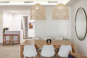 A modern kitchen with white cabinets, a stainless steel refrigerator, and a dining area with a wooden table and white chairs. - INf12A- Apartment close to beach and old town (Estepona)