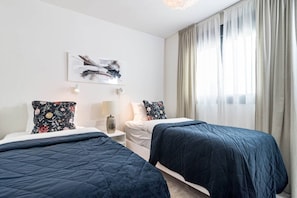 Ein Hotelzimmer mit zwei Betten, einem Nachttisch, einer Lampe und einem Fenster mit Vorhängen.