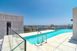 A rooftop swimming pool with clear blue water, a glass balustrade, and a view of the city and sea. - INF26H- Comfortable and spacious city apartment (Estepona)