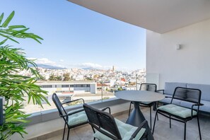 A balcony with a table and chairs, overlooking a cityscape with buildings and mountains. - INf26F - Modern and bright city apartment (Estepona)