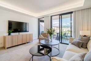 A modern living room with a flat-screen TV, a round coffee table, a sofa, and a balcony with a city view. - INf26F - Modern and bright city apartment (Estepona)
