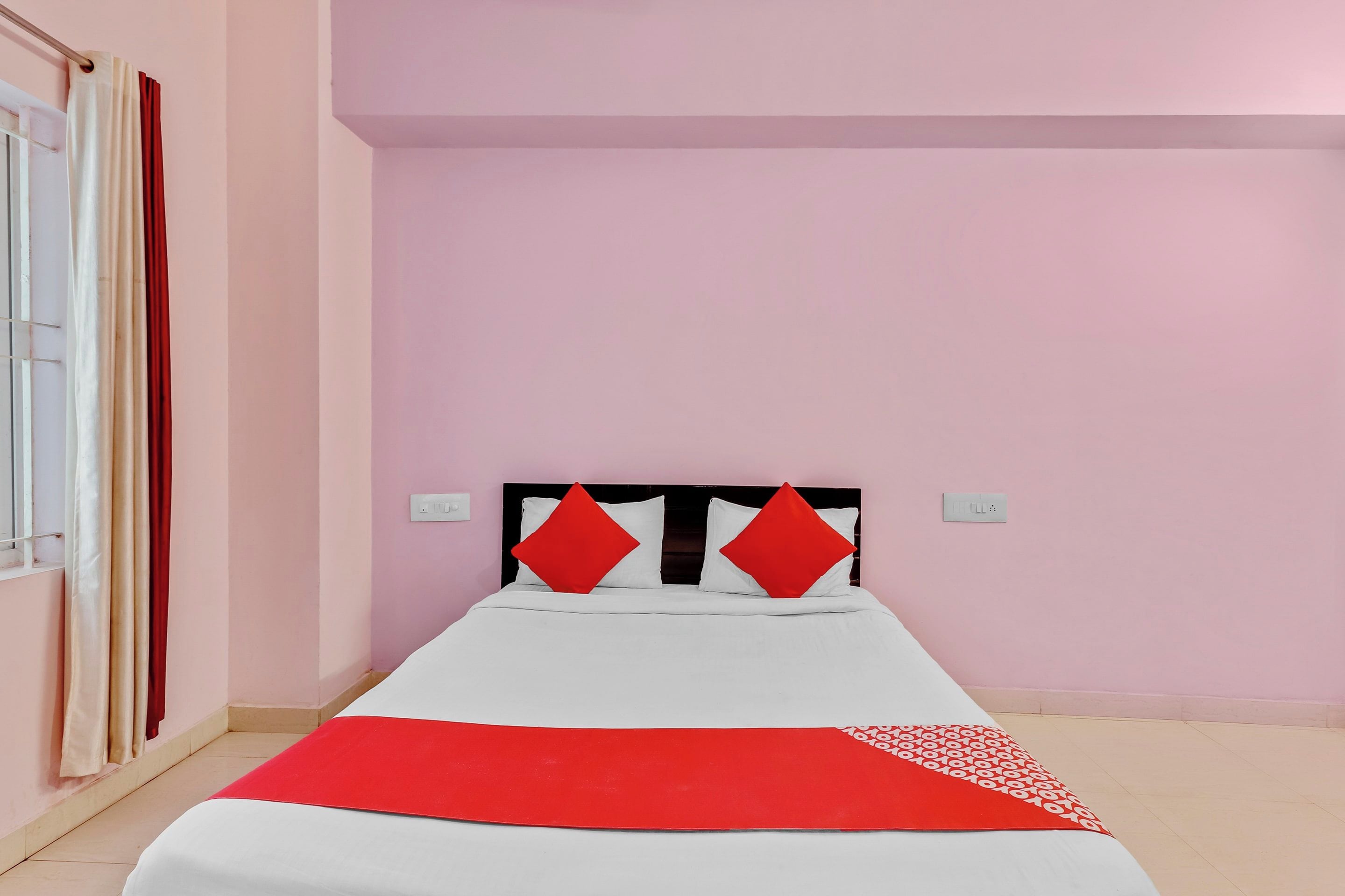 Una cama individual con una colcha blanca y roja, dos almohadas rojas y un cojín decorativo rojo en el cabecero.