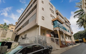 Un edificio de varios pisos con balcón, escalera y un automóvil estacionado.