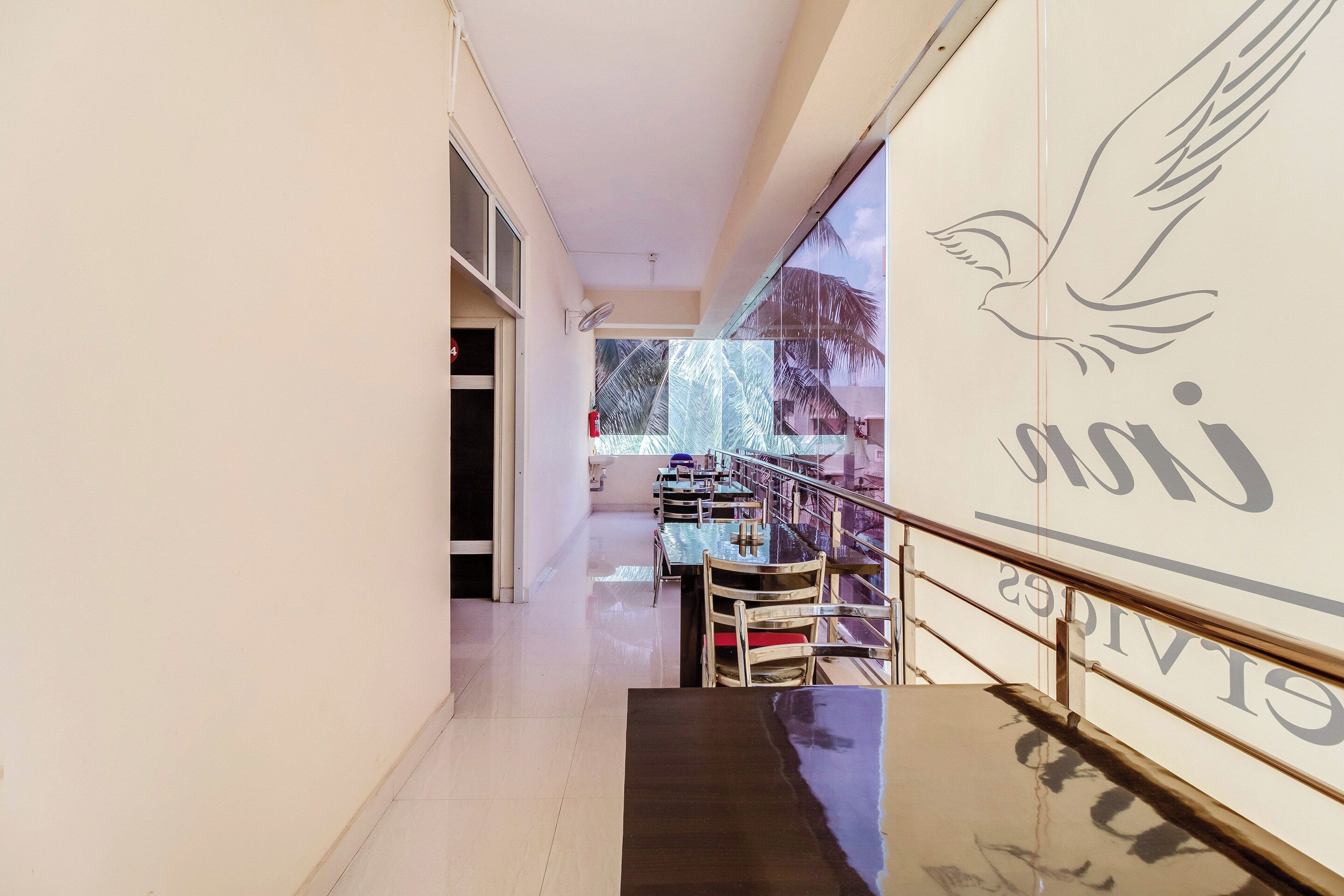 A corridor with a dining area featuring tables and chairs, a staircase, and a wall with a bird and text.