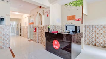 Een hotel receptie met een receptiebalie, een brandalarm en een bordje met informatie over de dienstverlening van het hotel.