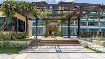 Um edifício moderno com entrada coberta, degraus que levam à entrada e área de jardim com plantas e uma pérgula.