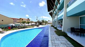 Piscina com borda em azulejo, ao lado de um edifício com varanda e área de estar externa.