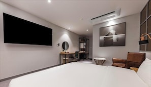 A modern hotel room with a large bed, a desk with a chair, a round mirror, a small round table, a sofa, and a flat-screen TV mounted on the wall. - Hotel about (Cheongju)