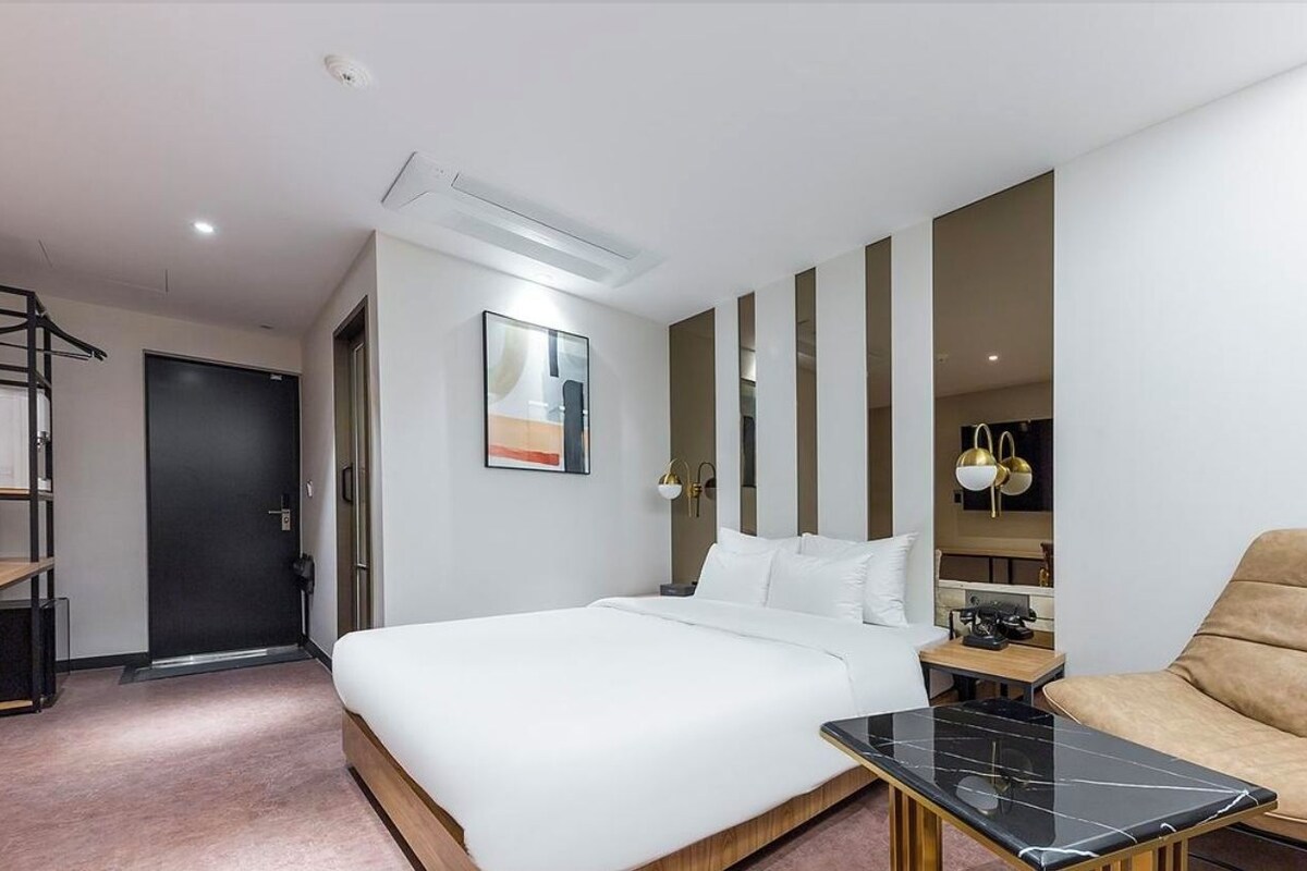 A hotel room with a bed, a sofa, a small table, a door, and a wall-mounted artwork.