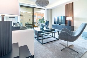 A modern living room with a sofa, coffee table, and a grey armchair. There is a flat-screen TV mounted on the wall and a large window providing a view of the outside. - IN33K- Stunning city apartment close to beaches (Estepona)