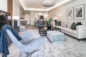 Ein modernes Wohnzimmer mit Sofa, Sessel, Couchtisch und einem Essbereich im Hintergrund.