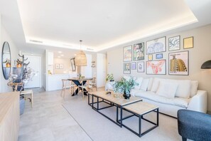A modern living room with a sofa, coffee table, and dining area. - INf34I - Modern & bright city apartment (Estepona)