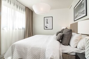 Ett hotellrum med en säng, gardiner, en hängande lampa och inramade konstverk på väggen.
