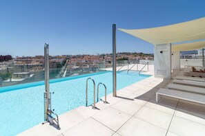En pool på taket med kristallklart blått vatten, ett glasräcke och utsikt över stadens silhuett.