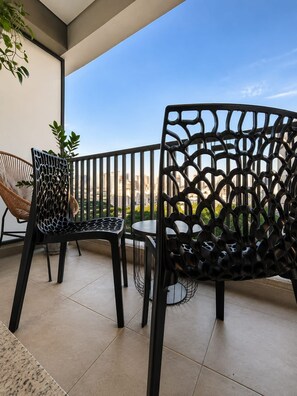 A balcony with two chairs, one with a woven backrest and the other with a geometric backrest, and a view of a cityscape. - SETIN 1610 (São Paulo)