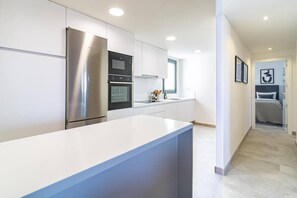 A modern kitchen with stainless steel appliances, a white countertop, and a view into a bedroom through an open door. - INf36K - Luxury apartment perfect location (Estepona)