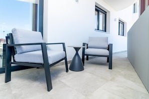 A modern outdoor seating area with two chairs and a table, a clear sky, and a building in the background. - INf36K - Luxury apartment perfect location (Estepona)