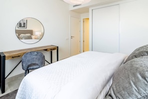 A bedroom with a bed, a desk, a chair, a round mirror, and a door. - INf36K - Luxury apartment perfect location (Estepona)