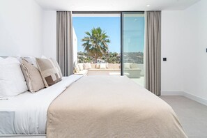 A modern bedroom with a large bed, a balcony with a view of palm trees and a cityscape, and a sliding glass door. - LAq75 - Beautiful Apartment with stunning view (Benahavís)