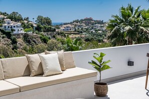 A rooftop terrace with a beige sofa, a potted plant, and a view of a coastal town. - LAq75 - Beautiful Apartment with stunning view (Benahavís)