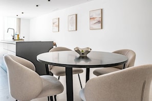 Een moderne eetruimte met een ronde tafel, vier stoelen en drie ingelijste kunstwerken aan de muur.