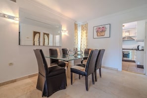 A dining area with a glass table and black chairs, a kitchen in the background, and a mirror on the wall. - LAlq13 Stunning Frontline Golf 3 bed apt (Benahavís)