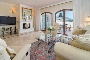 Un salón amplio con televisor de pantalla plana, chimenea, una mesa de centro de vidrio y un sofá.