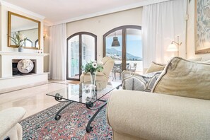 A living room with a sofa, a glass coffee table, a fireplace, and a view through large windows. - LAG - Spacious townhouse with private jacuzzi (Benahavis)