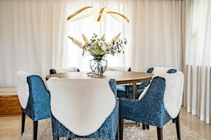 Una mesa redonda para comer con seis sillas, un florero con flores y una lámpara moderna.